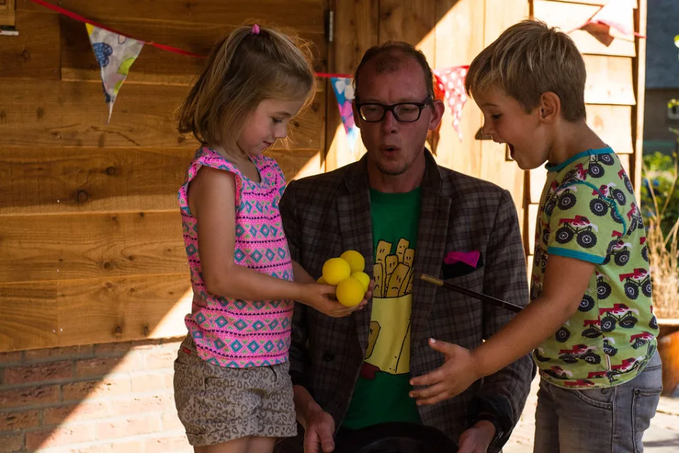 Lange Jan de Trucjesman goochelt met twee kinderen tijdens een kinderfeestje
