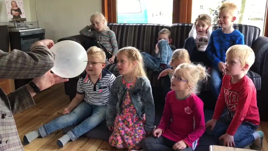 Kinderen op een verjaardagsfeestje in de woonkamer kijken gefascineerd naar een truc van Lange Jan