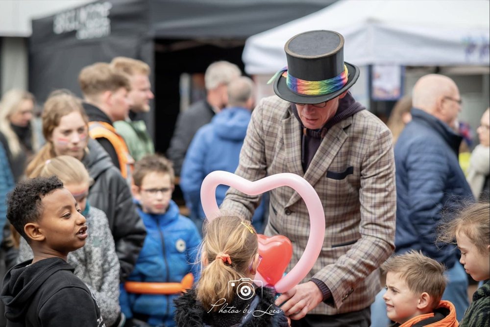 Lange Jan met hoge hoed maakt een ballonhart, omringd door kinderen