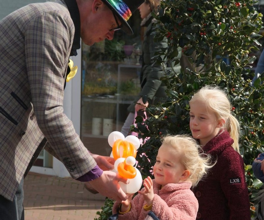 Lange Jan geeft een ballonkunstwerk aan een blij klappend meisje