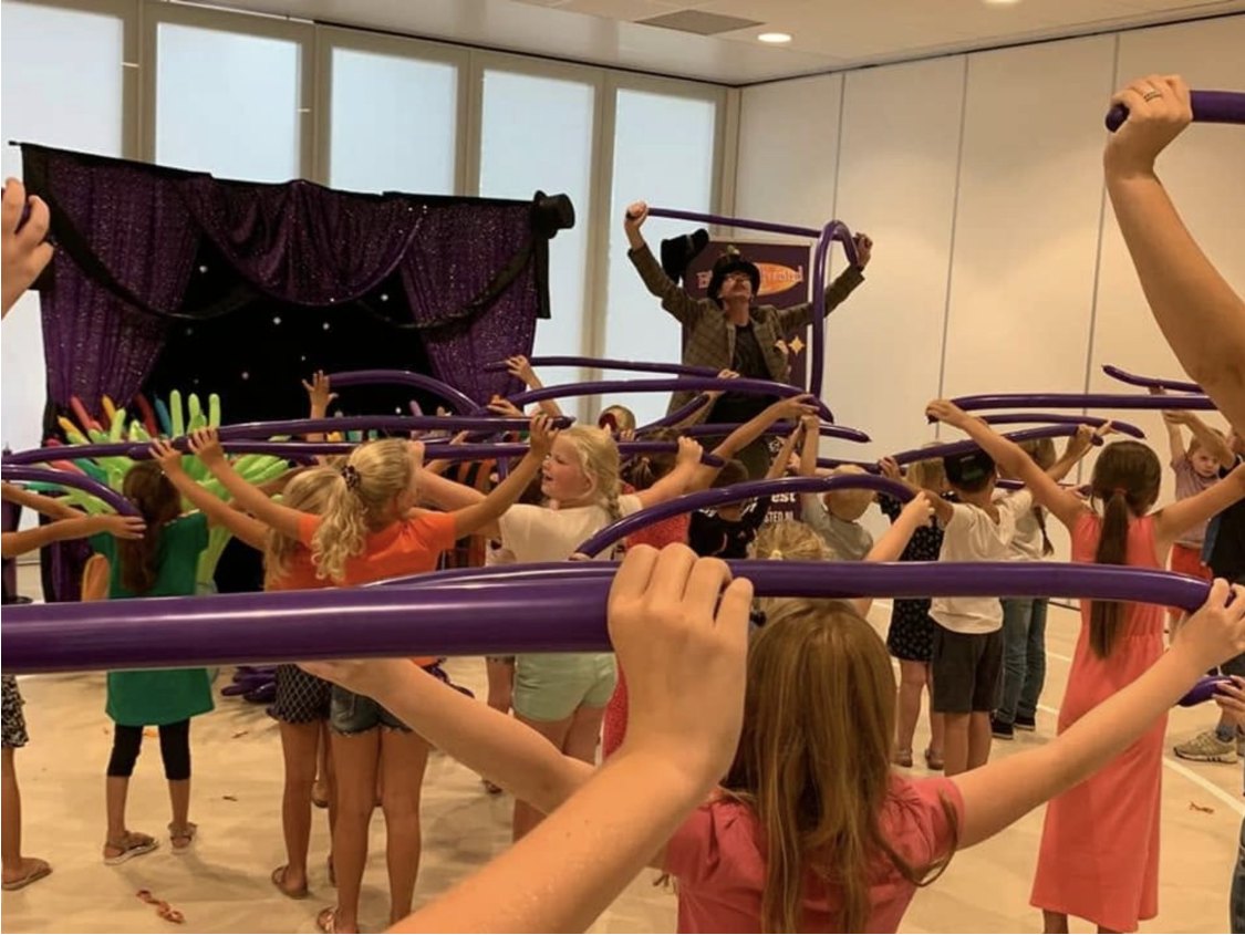 Lange Jan op het podium met een groep kinderen die lange paarse ballonnen omhoog houden